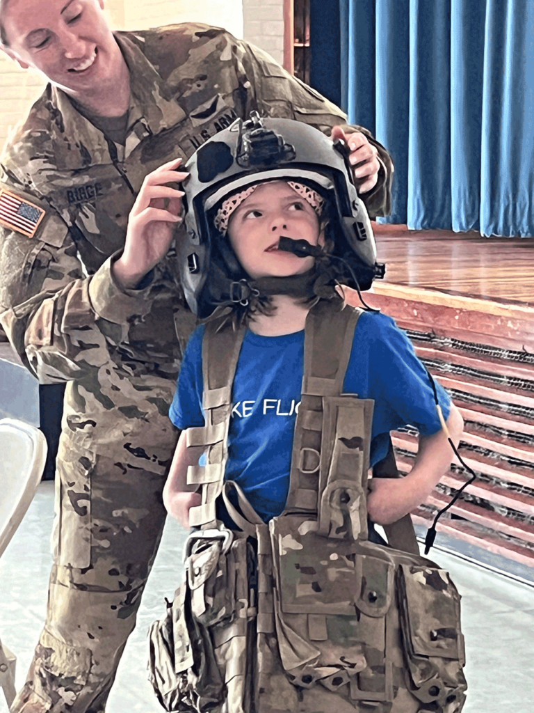 Female second grade student trying on pilot's helmet and vest.