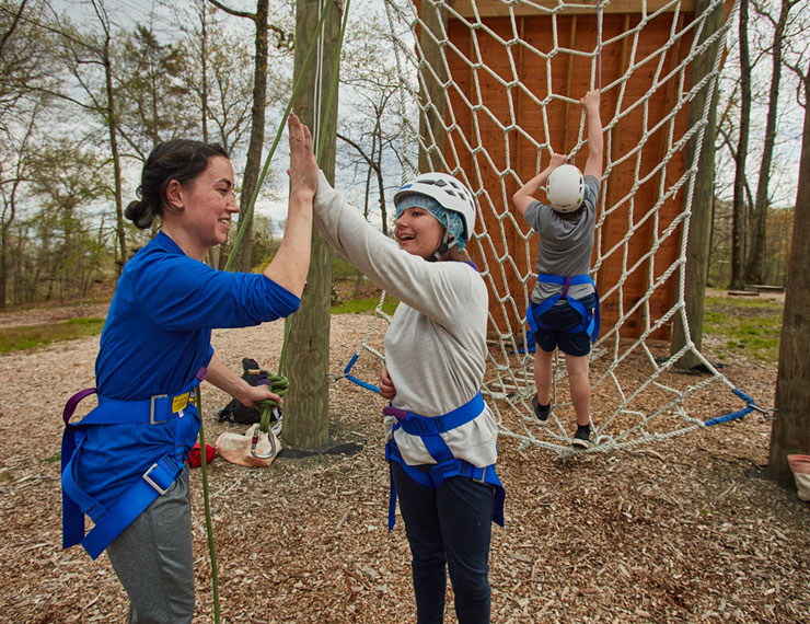 Teacher giving student high five before climbing high ropes element on challenge course