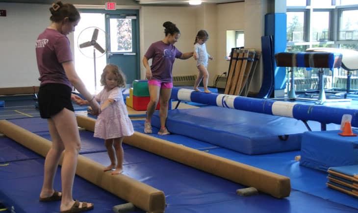 Camp counselors helping two small girls on balance beam