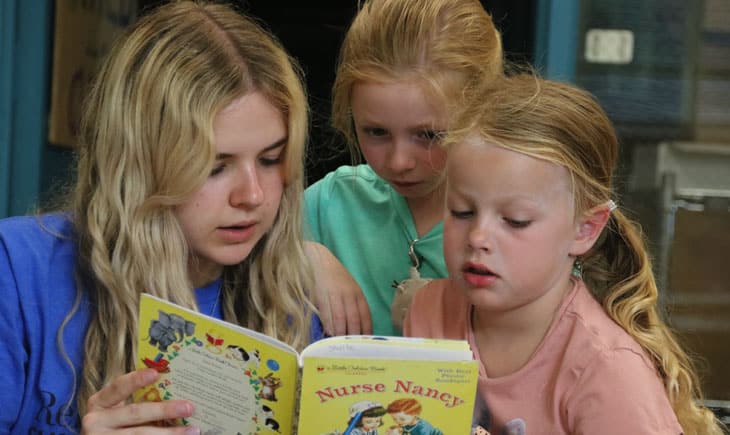 Camp Counselor reading a book to two girls