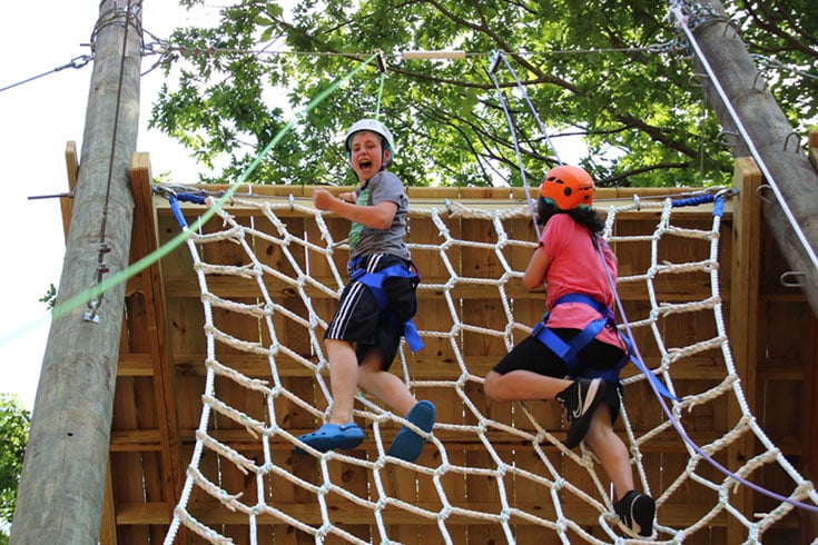 Two teens climbing rope wall at Challenge Course