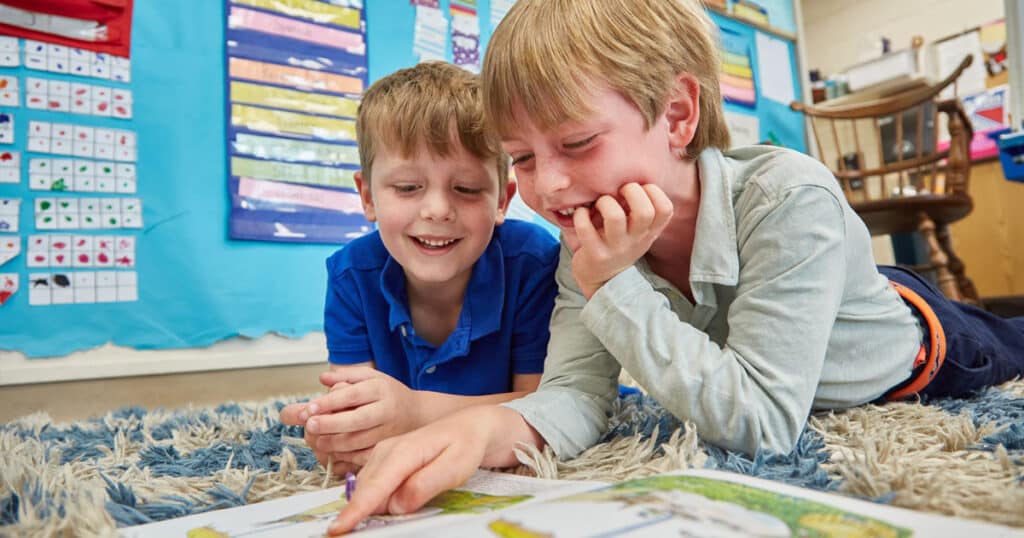 2 boys smiling laying on rug reading a book
