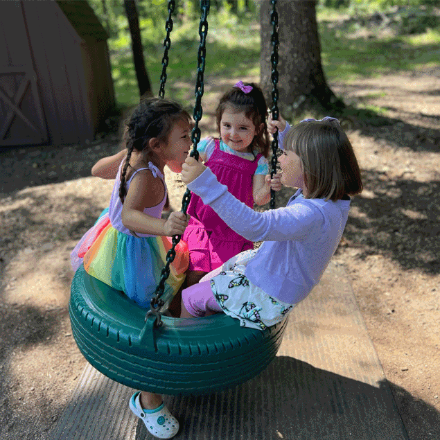 Three little girls playing on a tire swing