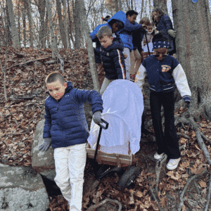 Group of third-grade students pulling covered wagons through the woods