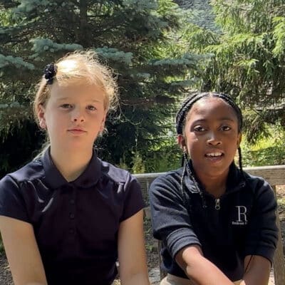 two girls, one white and one black, sitting on bench in butterfly garden