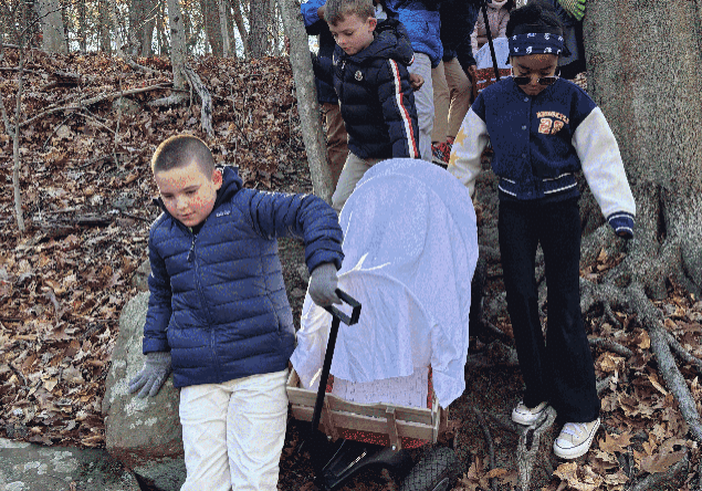 Group of third-grade students pulling covered wagons through the woods